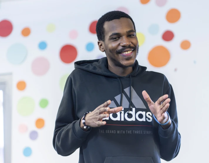 Young man smiling while making expressive hand gestures in front of a colorful polka-dot wall. Young man smiling while making expressive hand gestures in front of a colorful polka-dot wall.